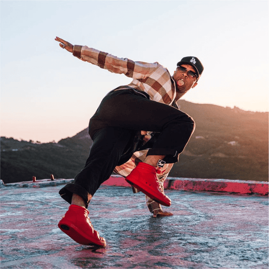 Dancer performs a dynamic floor move outdoors at sunset wearing red Fuego high-top sneakers, with one foot lifted to show the sole and pivot point during motion.